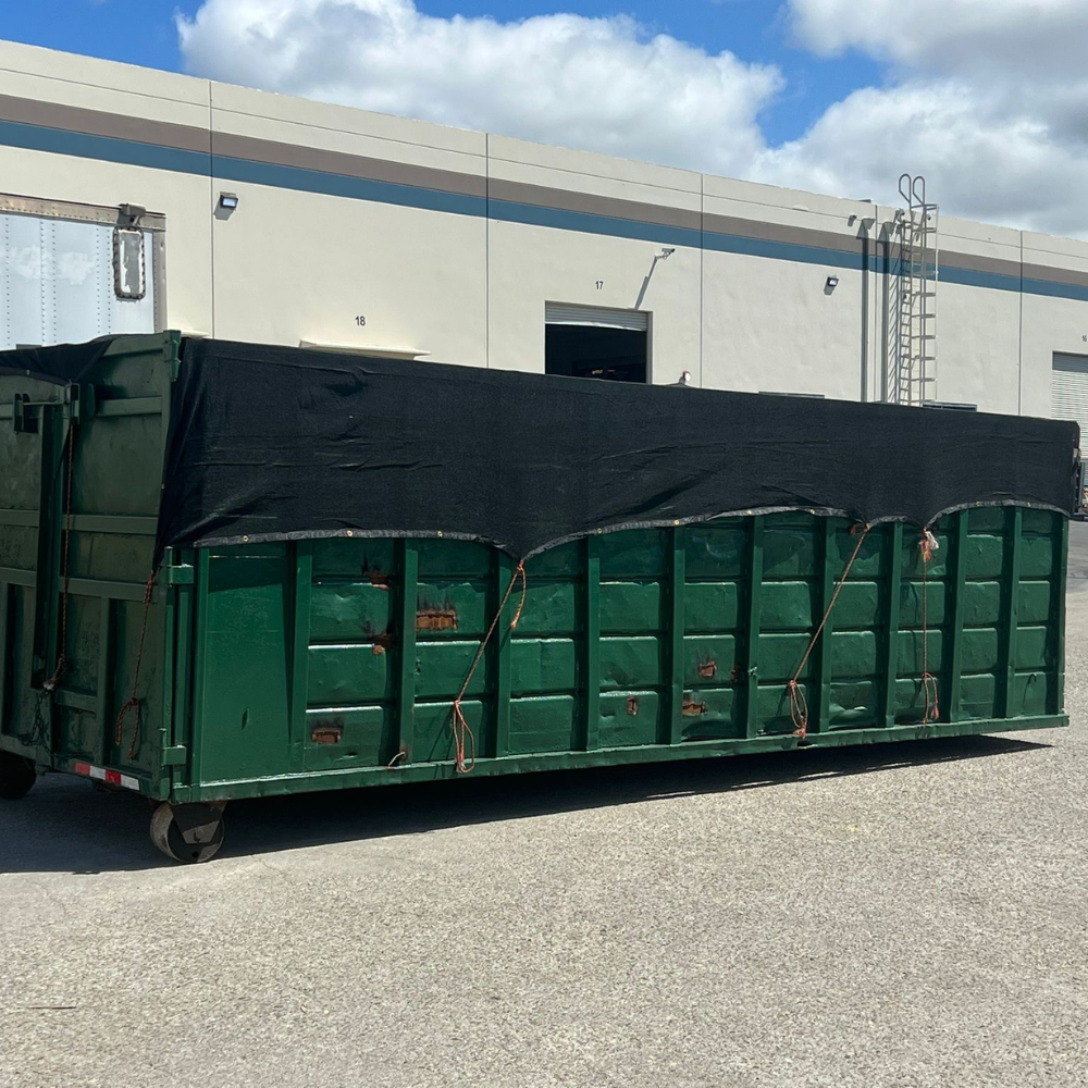 Green roll-off covered with a tarp on an industrial lot
